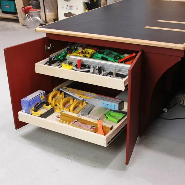 Woodworking table cabinet with open drawers holding router table accessories and woodworking tools.