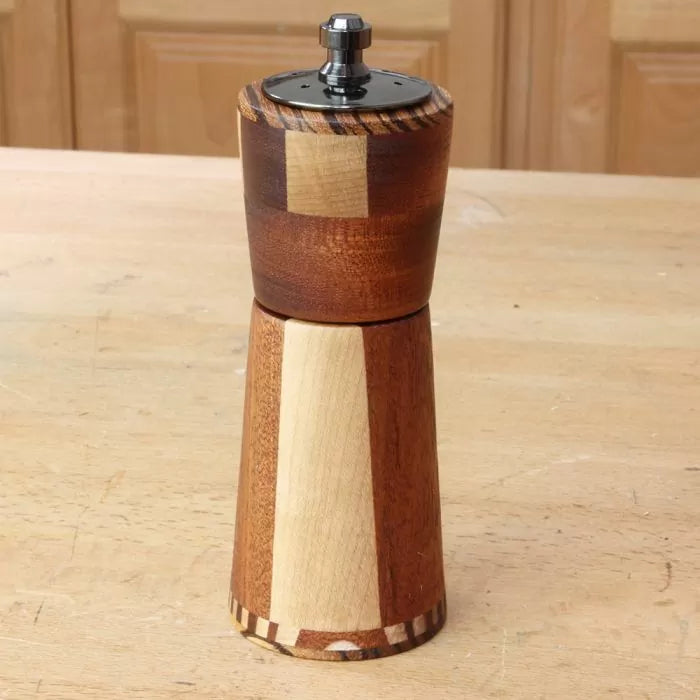 Handcrafted wooden pepper mill with mixed wood tones on a woodworking table