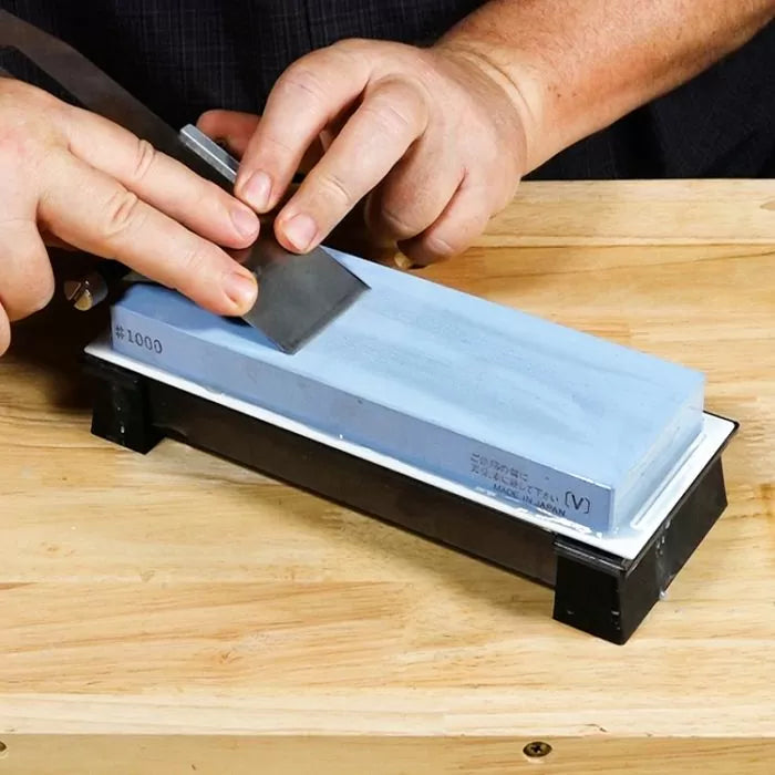 Sharpening a plane blade on a whetstone at a woodworking bench