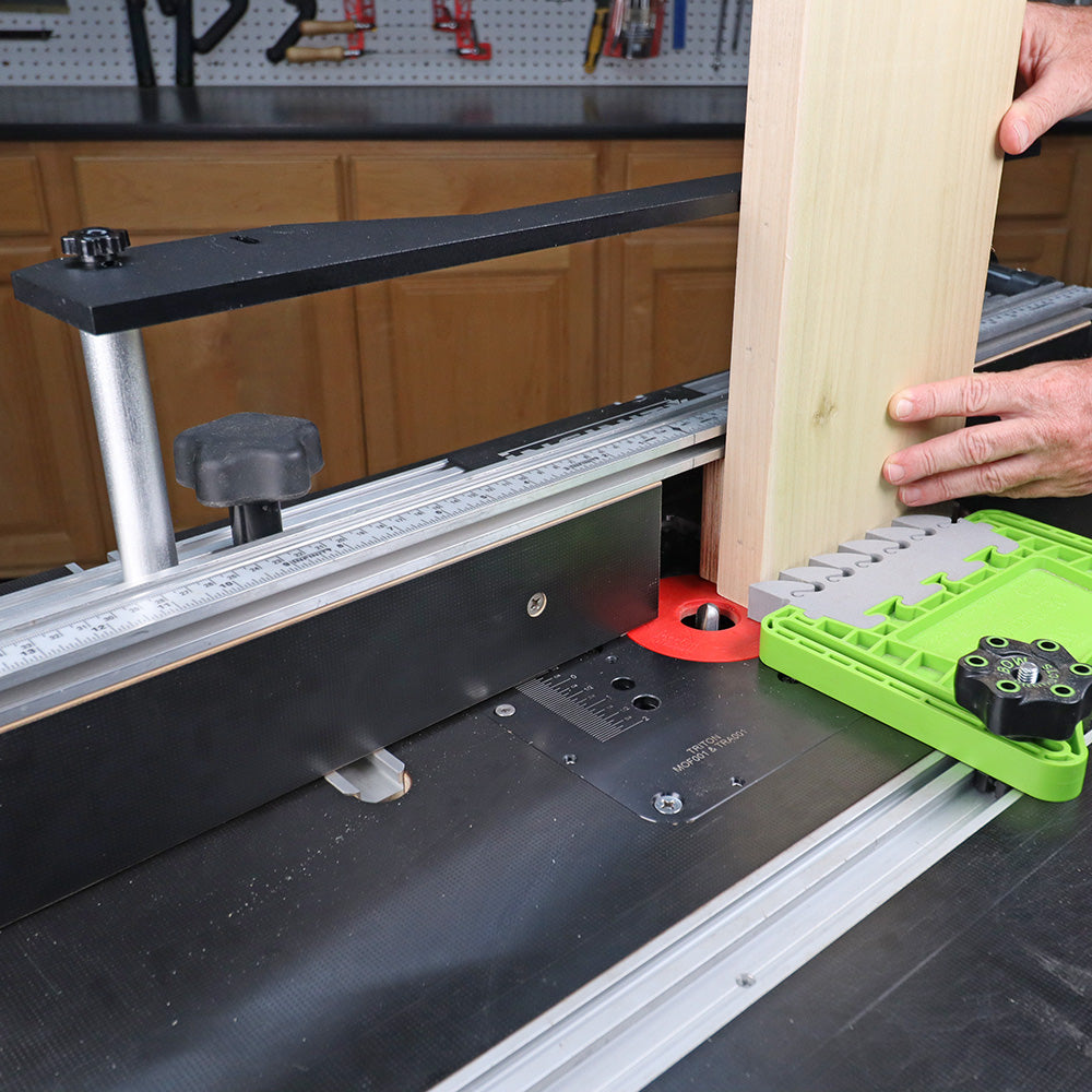 Woodworker using a router table with fence, push block, and guide to shape a wooden board.