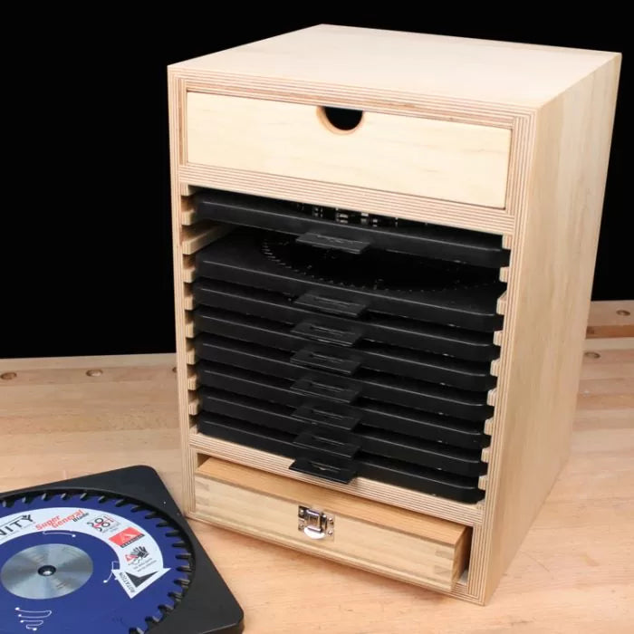 Wooden saw blade storage box with multiple black slots and two drawers on a workbench