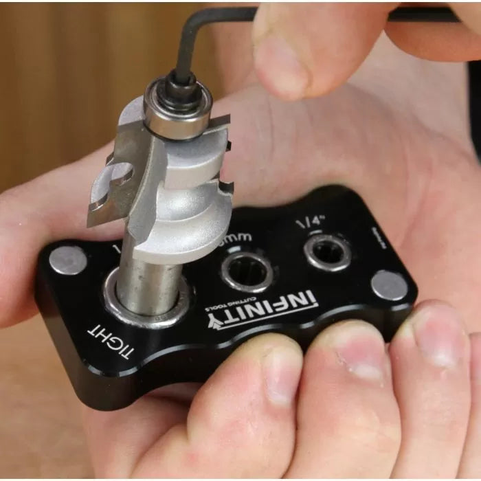 Person adjusting woodworking router bit with bearing using Allen wrench and setup jig