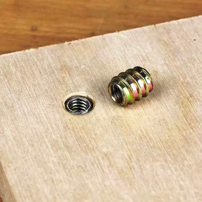 Threaded wood insert beside installed insert in plywood, woodworking hardware close-up