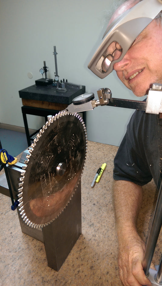 Person using a large wrench on a circular saw blade in a workshop setting.