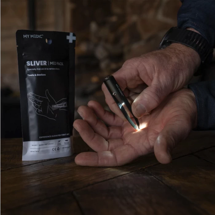 Person using illuminated tweezers from sliver removal first aid kit on hand, med pack nearby