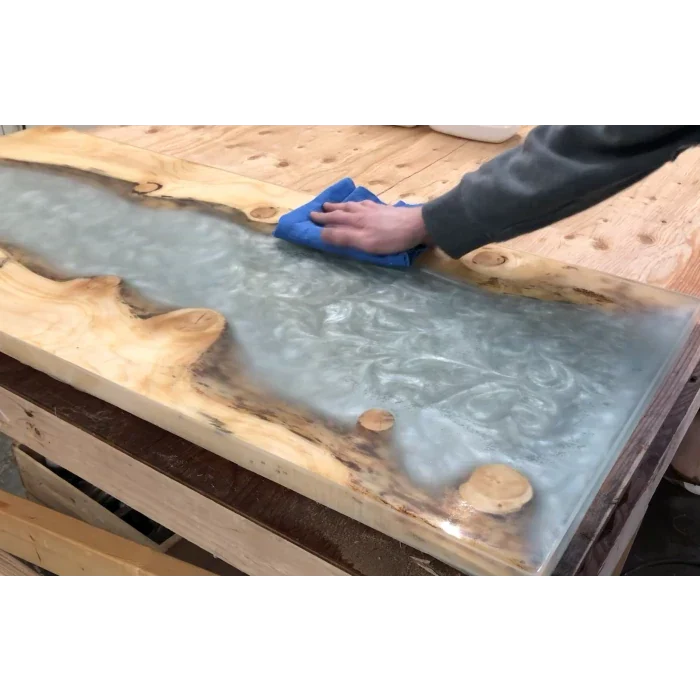 Hand polishing a live edge epoxy resin river table on a woodworking bench