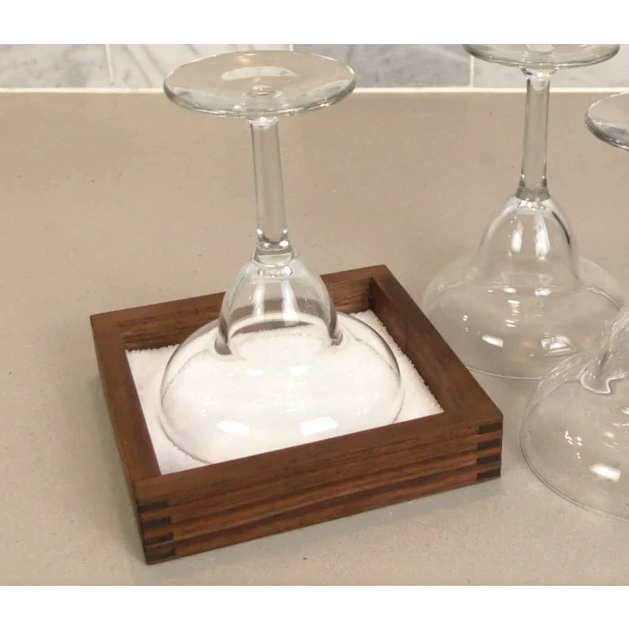 Stemmed wine glass upside down in a wood-framed salt rimmer on a kitchen counter