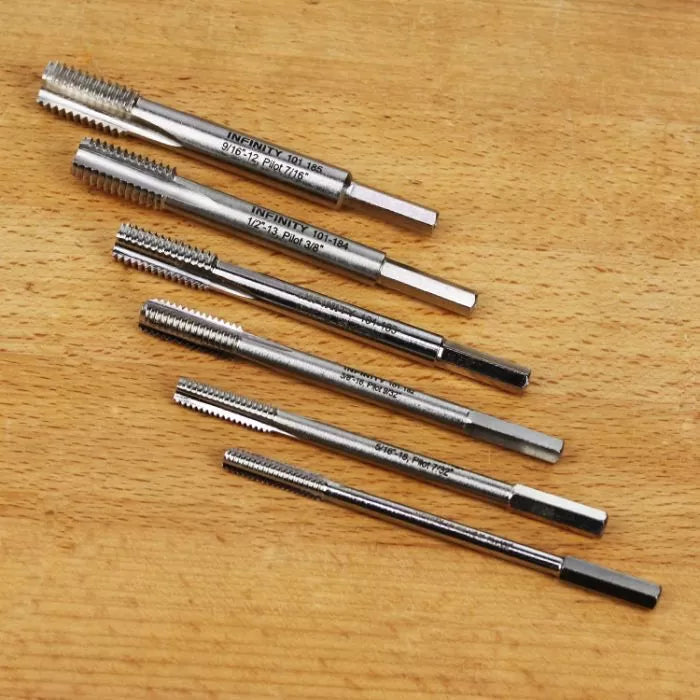 Set of six metal thread taps for woodworking on a wooden surface