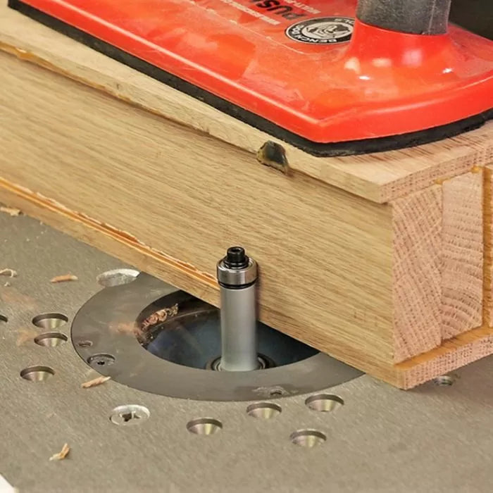 Straight router bit cutting wood on router table with red push block for woodworking