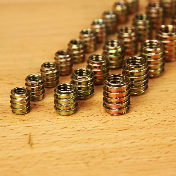 Threaded inserts for wood arranged on a wooden surface, various sizes shown.
