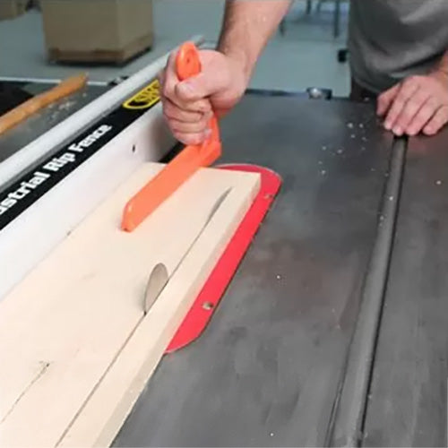 Woodworker using push stick to guide wood through table saw for precise cutting