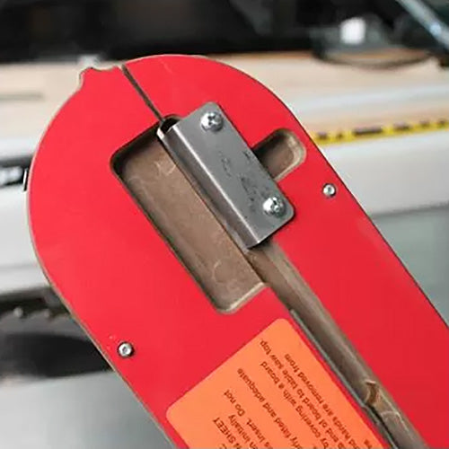 Table saw insert with steel hinge and safety label in a woodworking workshop setting