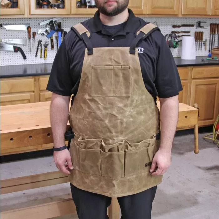 Man wearing a heavy-duty canvas woodworking tool apron with multiple pockets in a workshop