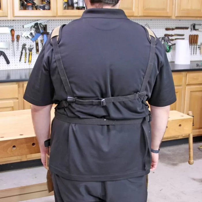 Person wearing a black tool apron with cross-back straps in a woodworking shop