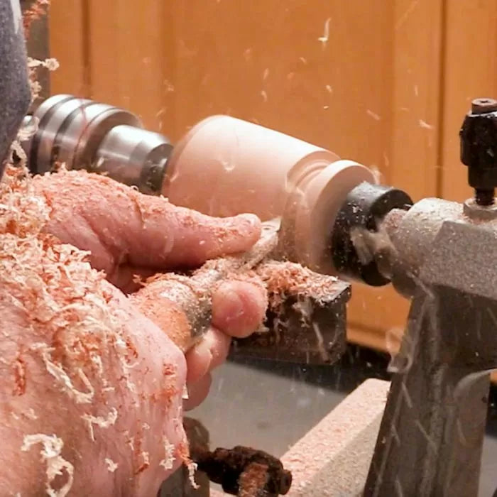 Woodworker using turning tool on a lathe with wood shavings flying in workshop