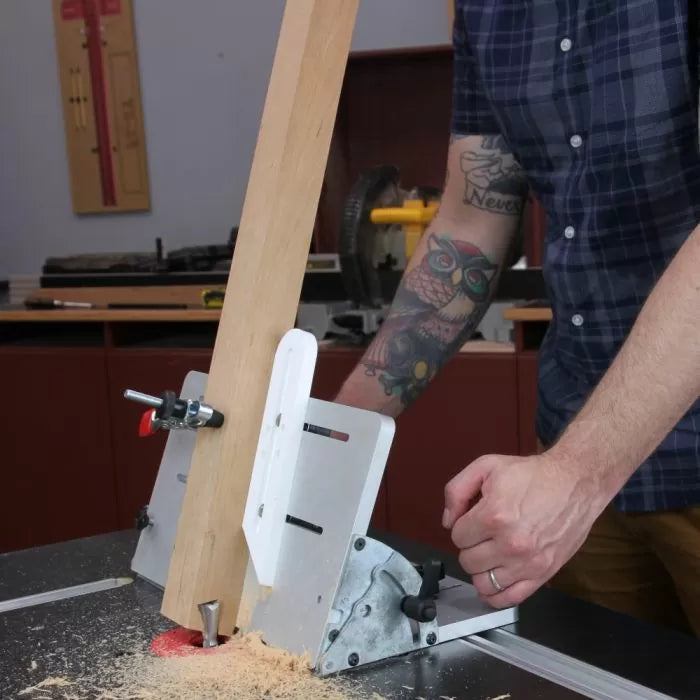 Woodworker using a table saw tenoning jig to cut a vertical board in a workshop.