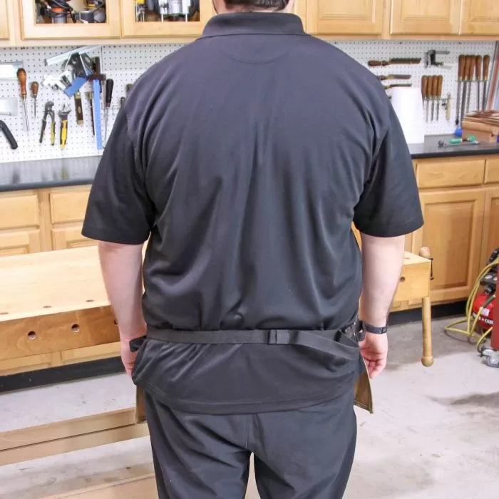 Rear view of person wearing a black waist tool apron in a woodworking shop.