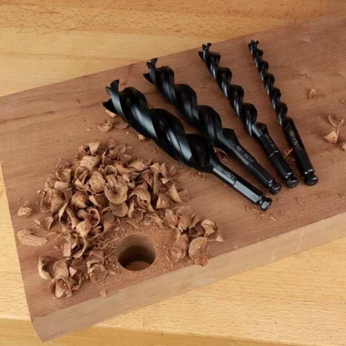 Set of black auger drill bits on wooden board with wood shavings and drilled hole