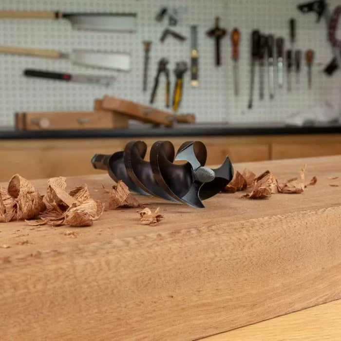 Close-up of auger drill bit on wood bench with wood shavings in woodworking shop