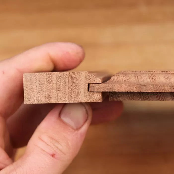 Hand holding two joined wood boards with a precise tongue and groove woodworking joint