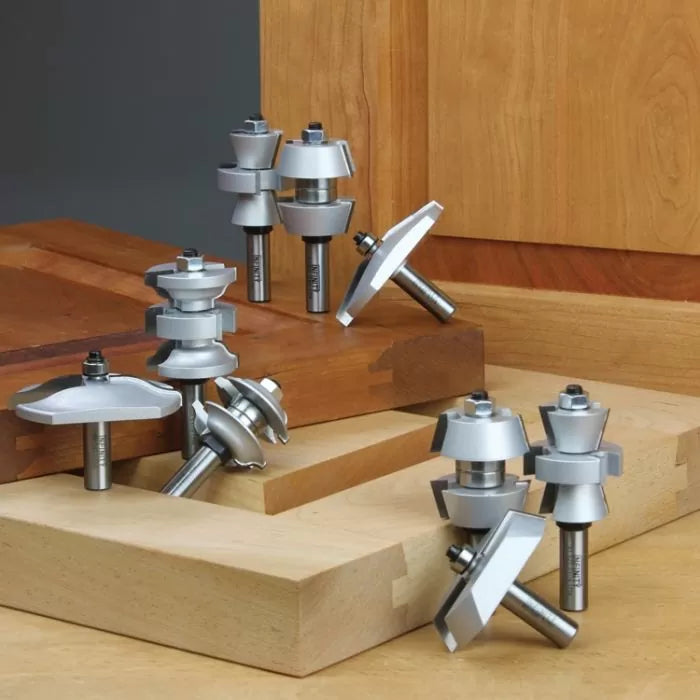 Assorted woodworking router bits displayed on wooden boards for joinery and edge shaping.