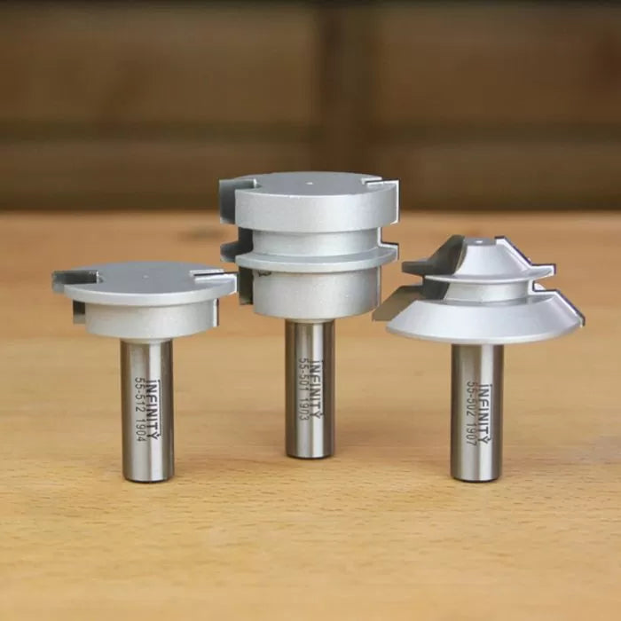 Three silver carbide-tipped router bits for woodworking on a wooden tabletop