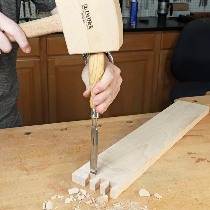 Woodworker using chisel and mallet to cut dovetail joints in a maple board