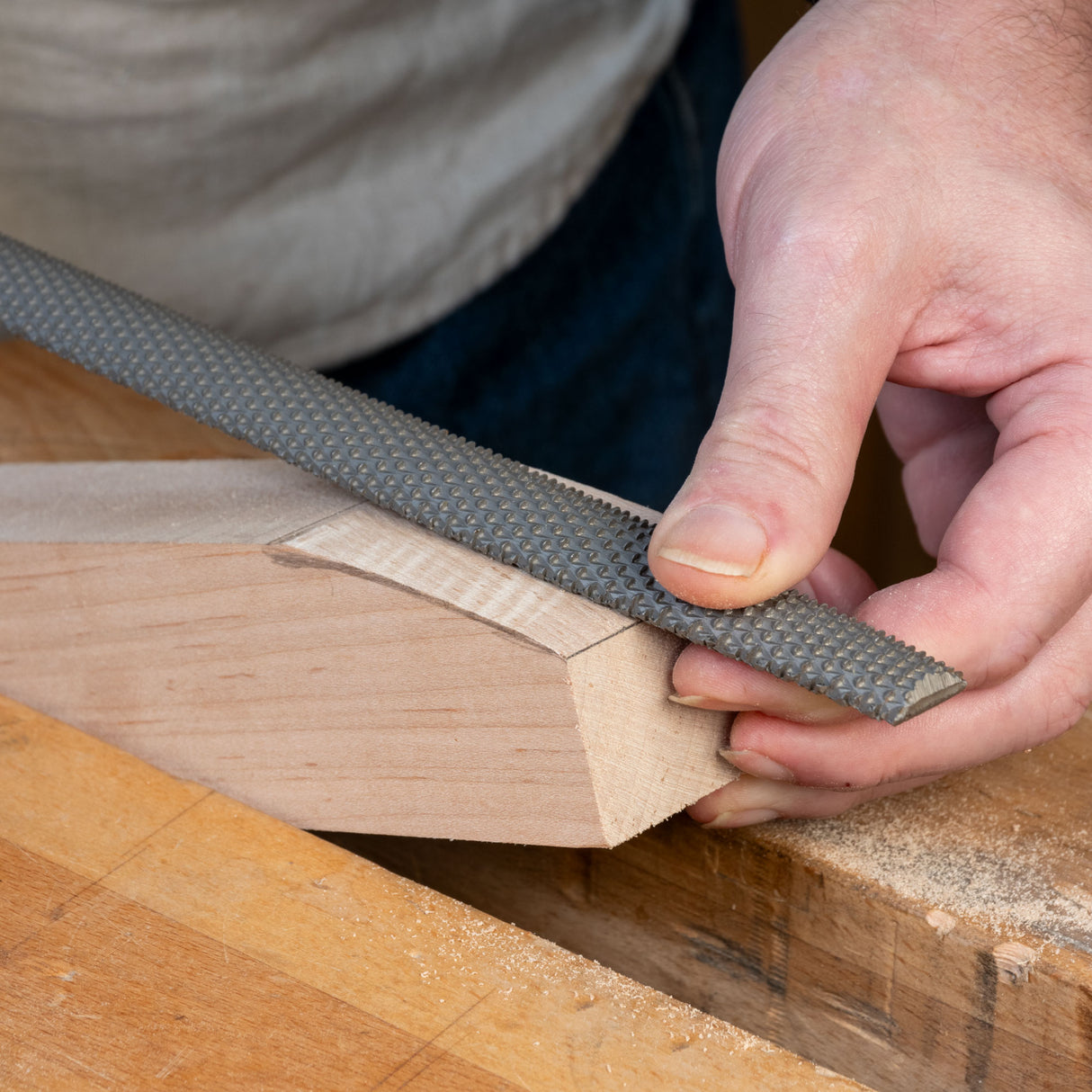 Hand using a premium rasp tool for woodworking on a shaped wooden block
