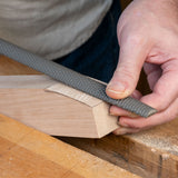 Hand using a premium rasp tool for woodworking on a shaped wooden block