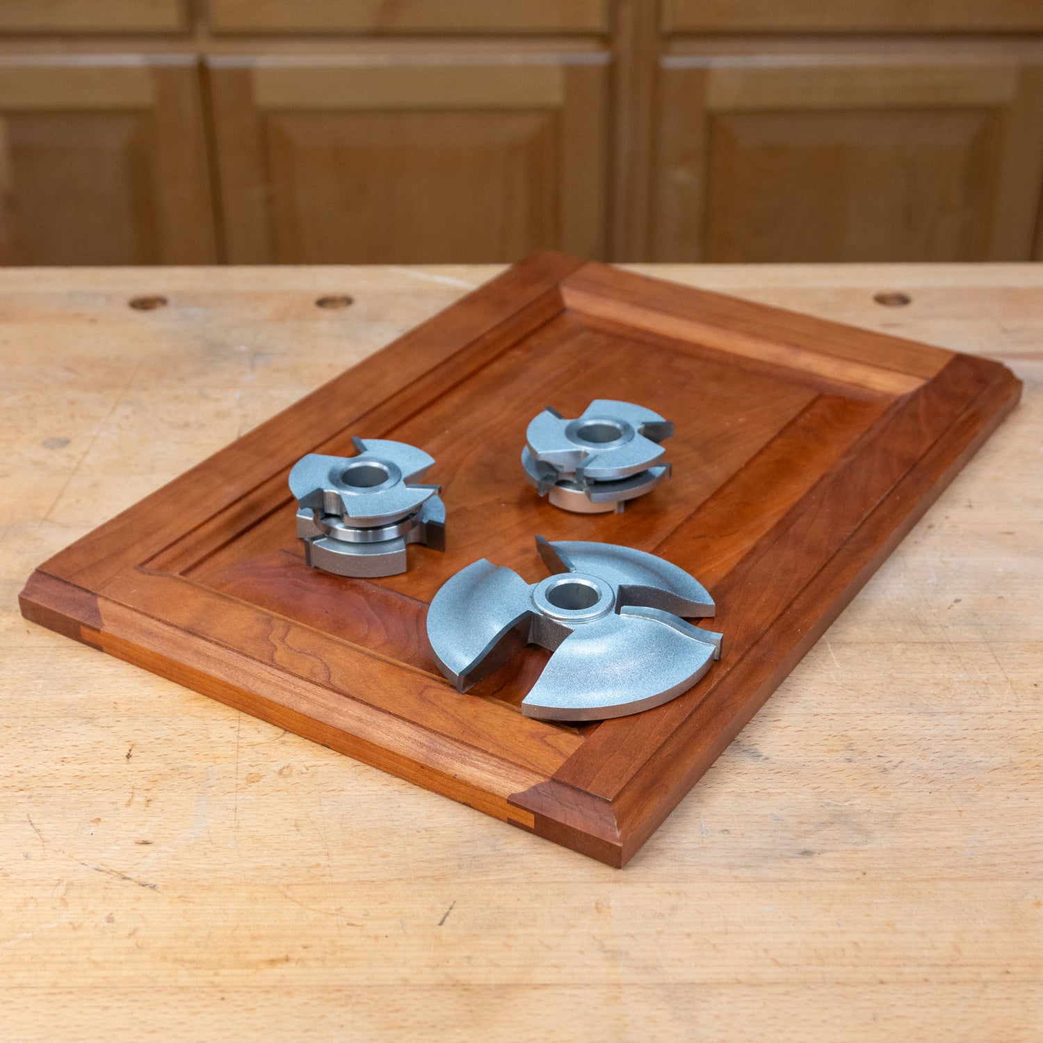 Ogee 3-piece cabinet door shaper cutter set on a wooden door panel, woodworking tools