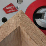 Close-up of a precise wooden miter joint with woodworking router table and bit in background