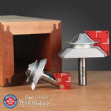 Lock miter router bits with red setup blocks on wood surface, next to a precisely joined wooden box.