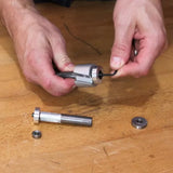 Hands assembling a woodworking router bit with bearing on a wooden workbench