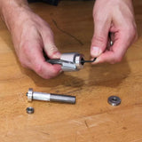 Hands assembling a woodworking router bit with hex key and bearings on a workbench