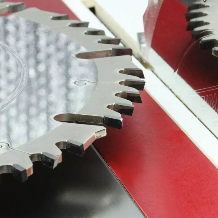 Close-up of a carbide-tipped table saw blade with sharp teeth on a red saw insert, woodworking tool.