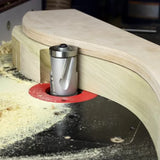 Router table with flush trim router bit cutting curved wood piece, surrounded by sawdust
