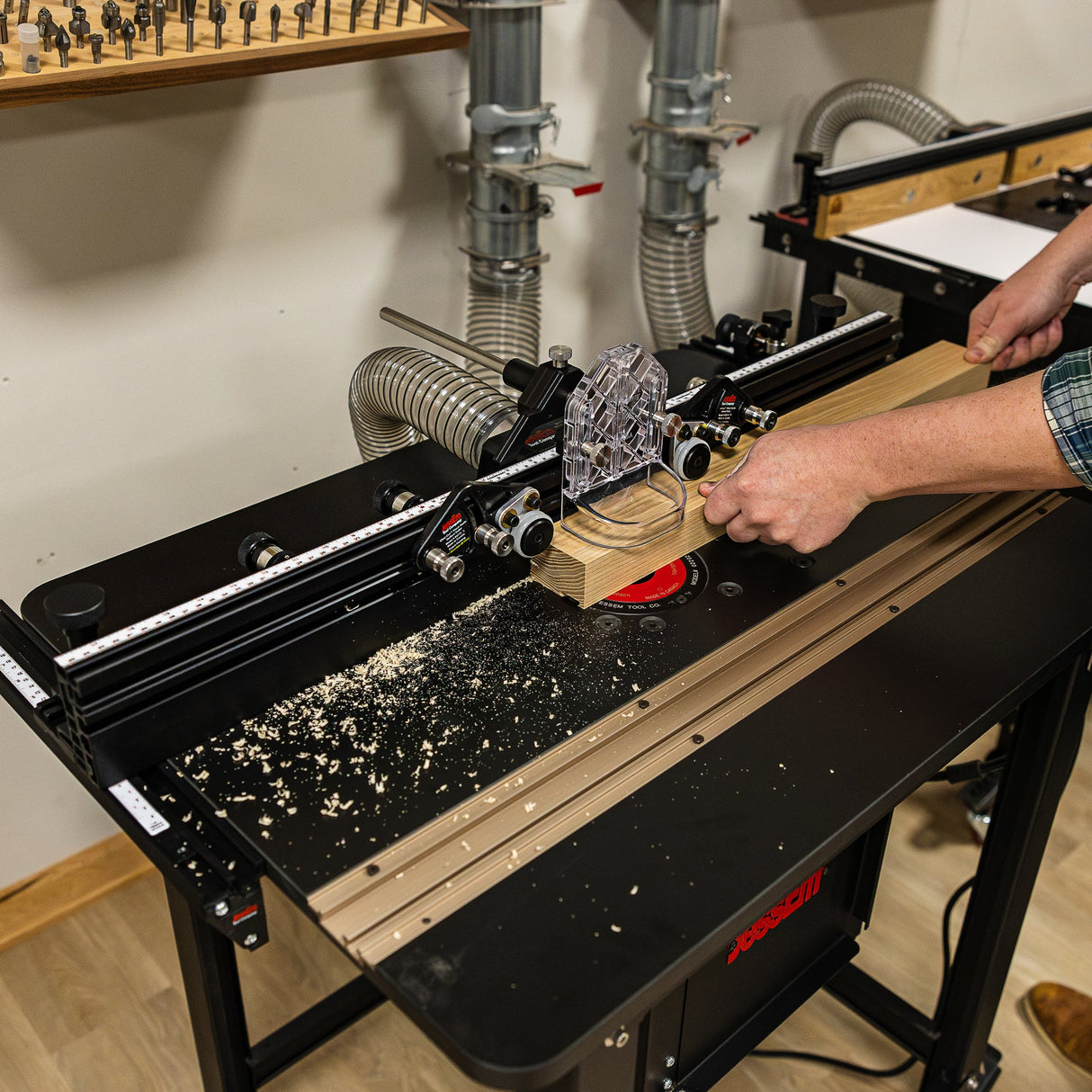 Woodworker using router table with dust collection, precision fence, and wood shavings visible.