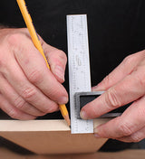 Person marking a wooden board with a pencil using a metal woodworking square ruler
