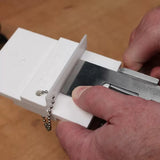 Hand holding woodworking plane blade in white honing guide on workbench