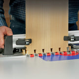 Woodworker using a router table jig to cut precise dovetail joints in a wooden board
