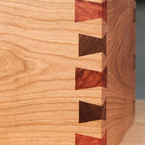 Close-up of a wooden box corner featuring precise dovetail joinery with contrasting wood inserts