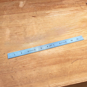 Stainless steel ruler with inch markings on a wooden workbench for woodworking measurement.