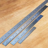 Set of four stainless steel woodworking rulers on a light wood workbench