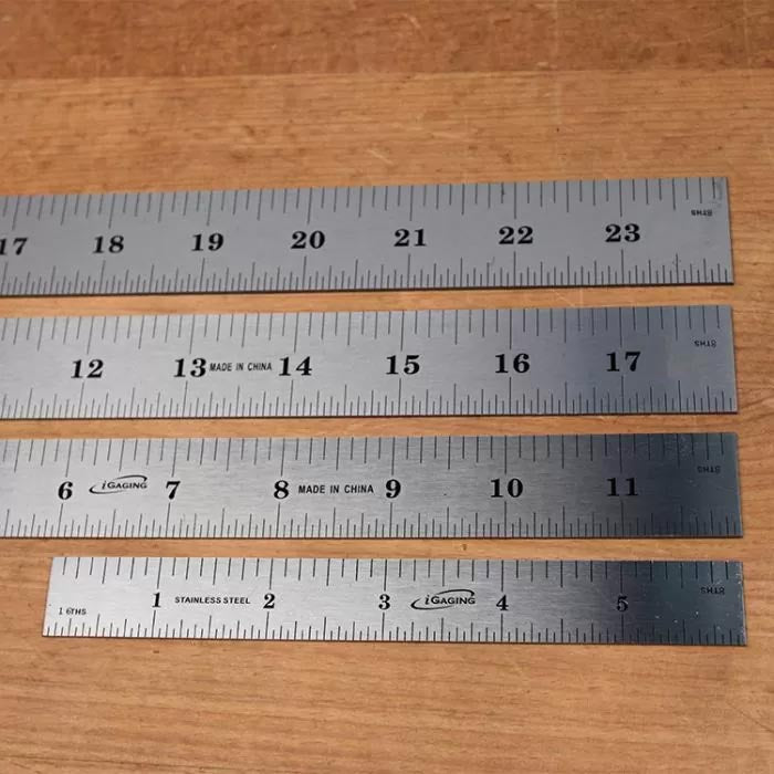 Set of four stainless steel rulers on wood surface, precise measuring tools for woodworking