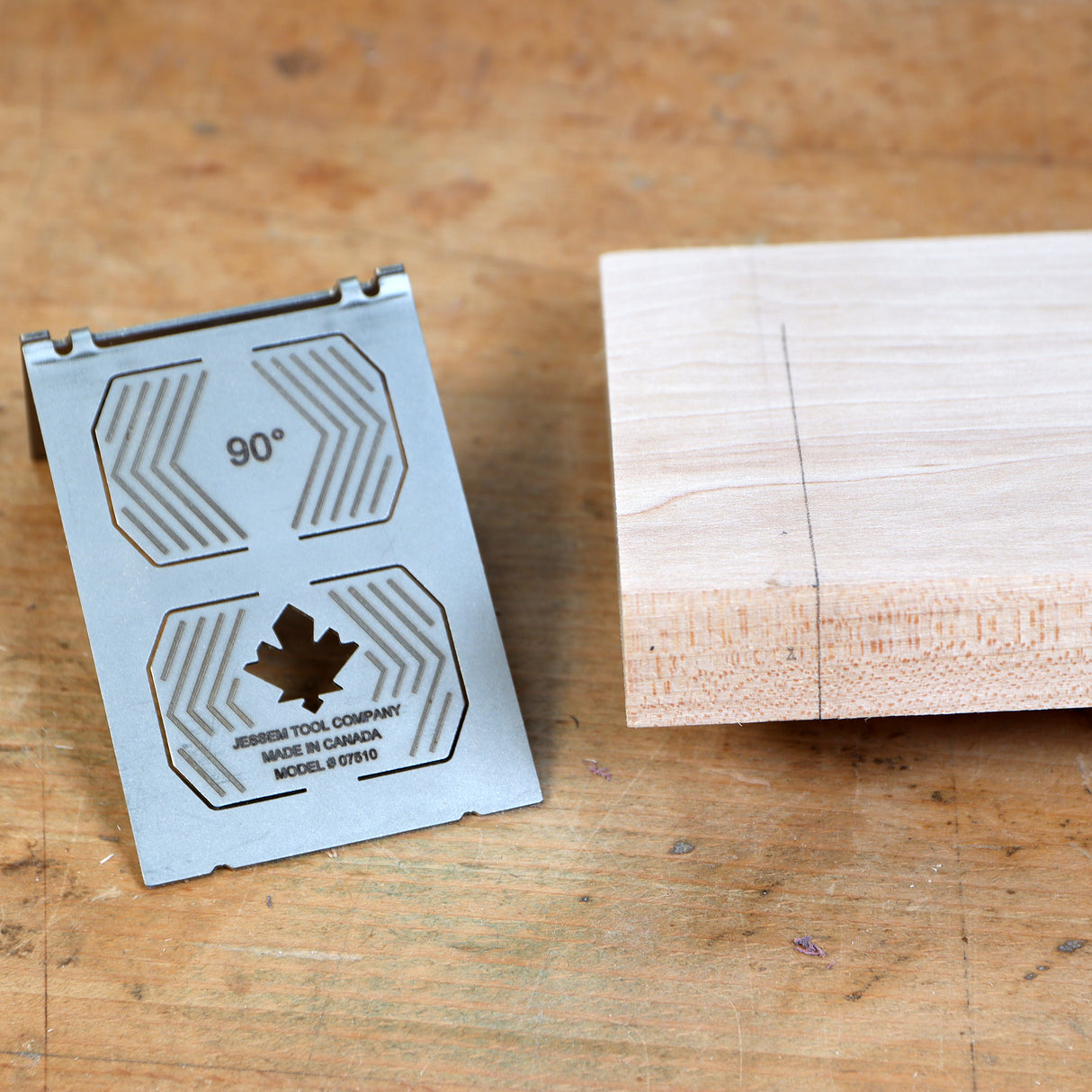 Metal 90-degree woodworking square beside marked wood block on workbench