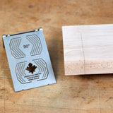 Metal 90-degree woodworking square beside marked wood block on workbench