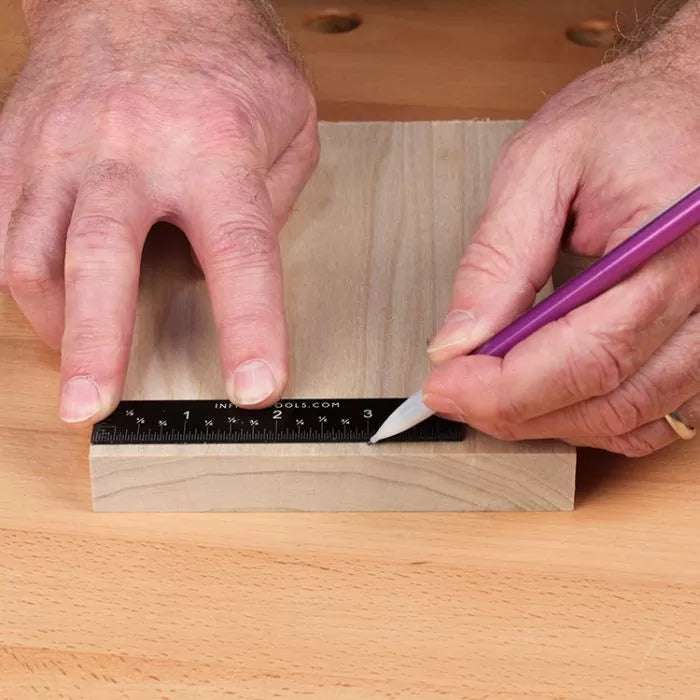 Marking a wooden board with a ruler and pencil on a woodworking bench