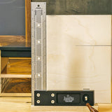 Precision woodworking square tool standing upright on a woodworking bench beside plywood