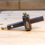Ebony marking gauge with brass accents on a wooden workbench for woodworking layout