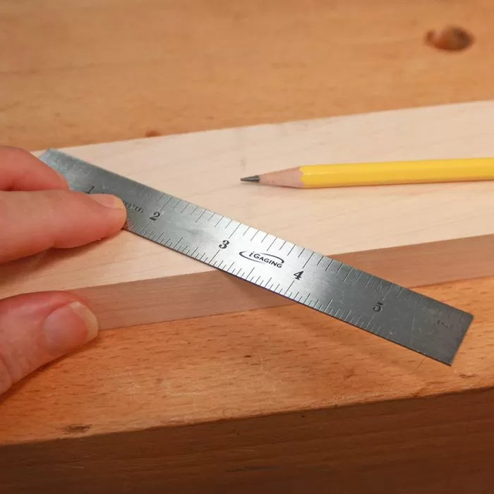 Stainless steel woodworking ruler and yellow pencil on a wooden workbench